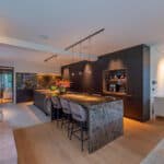 Crea Accent Interieur project G met By Eve Modular Pista Track Marbulito Suspension Minude (1) Strakke moderne keuken met zwart marmeren blad en warme verlichting.